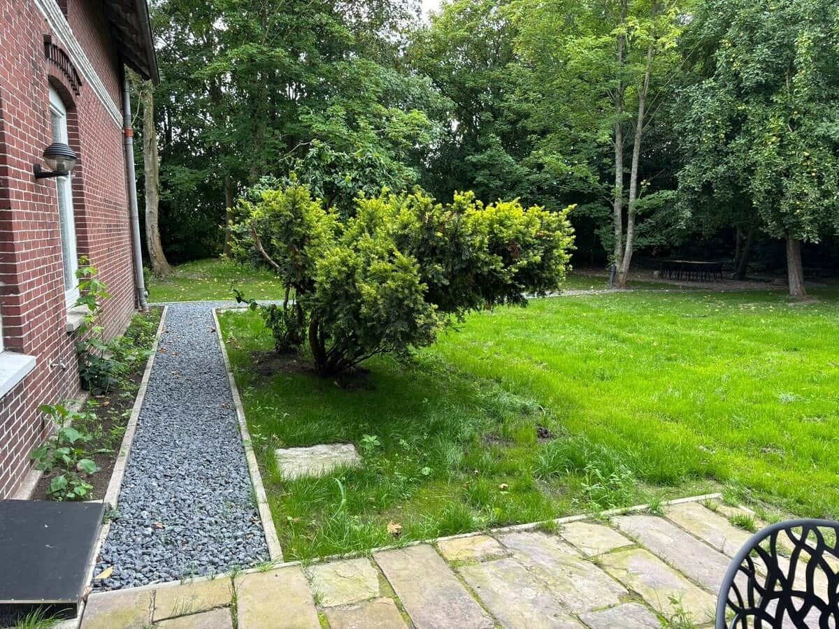 En have med grussti, græsplæne og en murstensbygning.