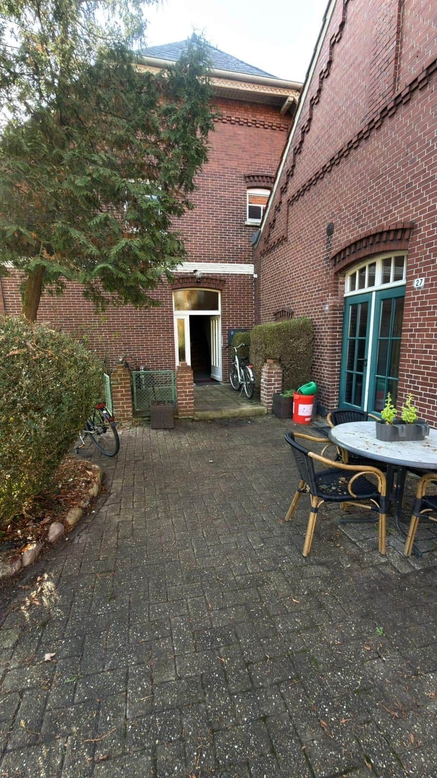 Ein Backsteinhaus mit einem gepflasterten Innenhof, einem Fahrrad, einem Tisch mit Stühlen und einer grünen Tür.