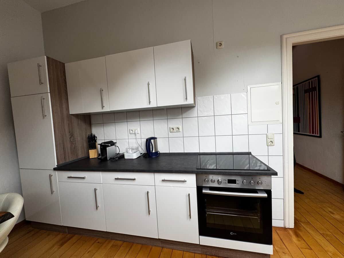 Eine Küche mit weißen Schränken, einer schwarzen Arbeitsplatte und einem eingebauten Backofen.