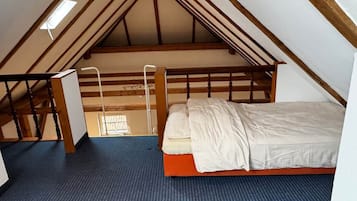 Ein Schlafzimmer mit schrägen Wänden, einem Bett, einer Leiter und einem Fenster.