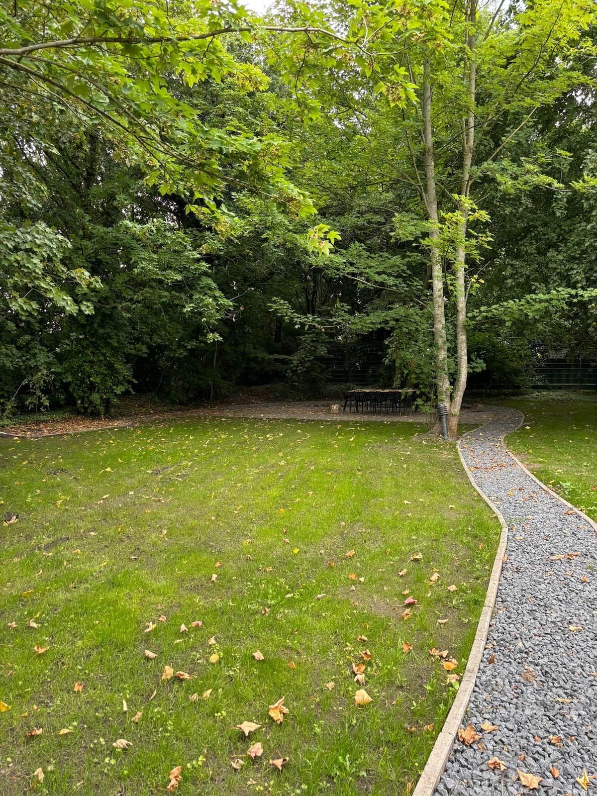 A grassy area with a gravel path, surrounded by trees.