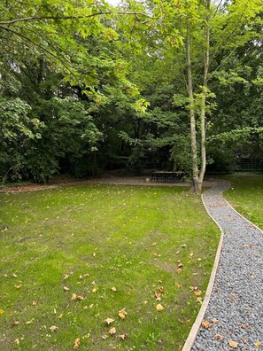 A grassy area with a gravel path, surrounded by trees.