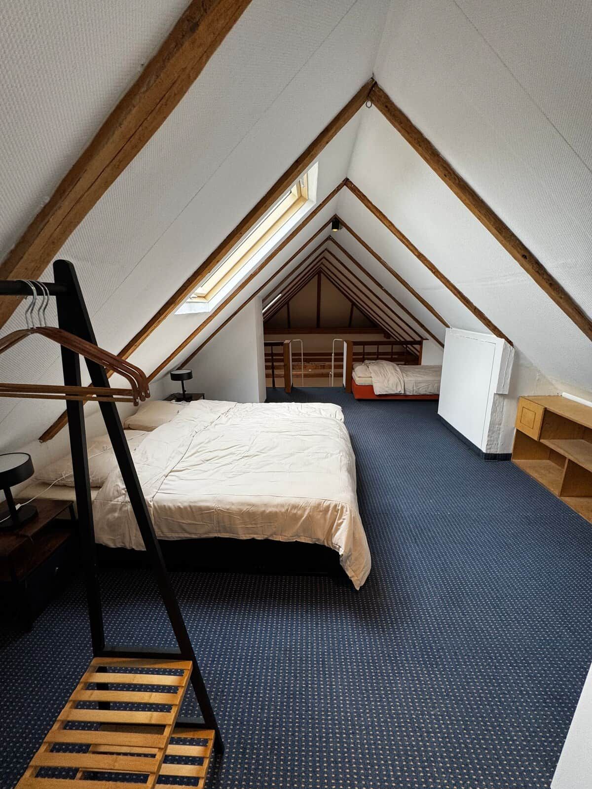 Ein Schlafzimmer im Dachgeschoss mit hohen Decken, geneigtem Dach, einem Bett, einem Schreibtisch und einem kleinen Fenster.