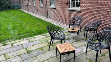 Une terrasse avec un sol en pierre, des sièges d’extérieur et un bâtiment en briques en arrière-plan.
