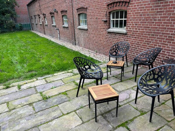 A patio with stone flooring, outdoor seating, and a brick building in the background.
