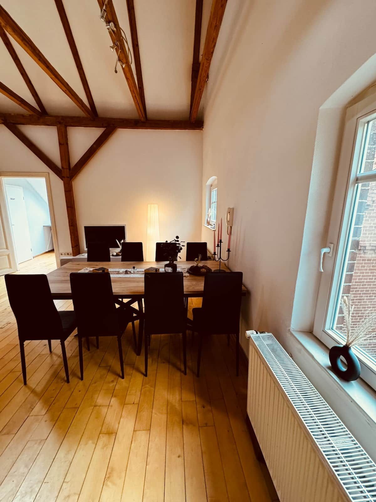 A dining area with a wooden table and chairs, a window with a view of a brick building, and a radiator on the wall.