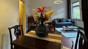 A dining area with a wooden table, chairs, a vase with flowers, and a hanging light fixture.