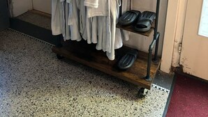 A hallway with a rack holding white robes and slippers, a Harmony tissue box, and a door with a sign.