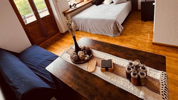 A bedroom with a bed, a bench, a table with decorative items, a painting, and a window with a view.