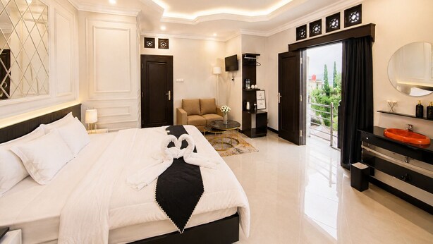 Habitación de hotel moderna con una cama grande, zona de estar, balcón y baño con espejo amplio y lavamanos.