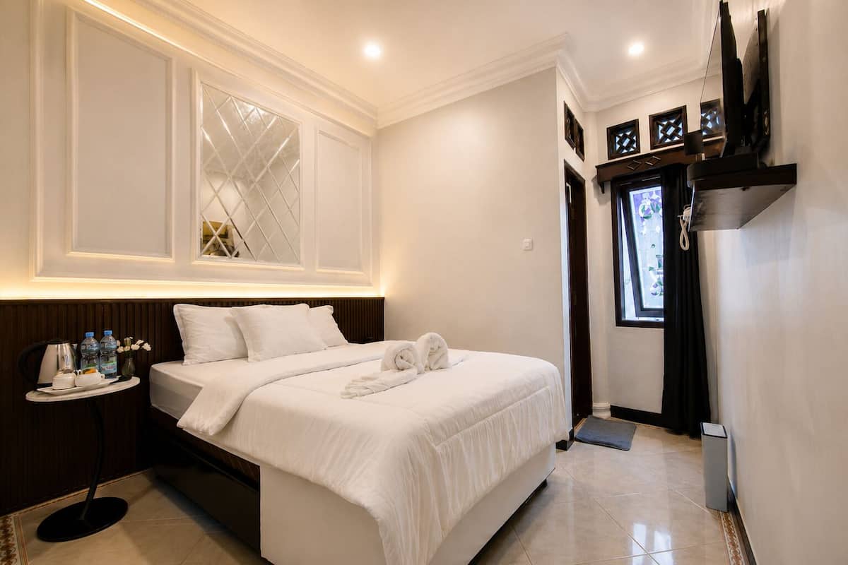 A hotel room with a bed, bedside table, and a TV mounted on the wall.