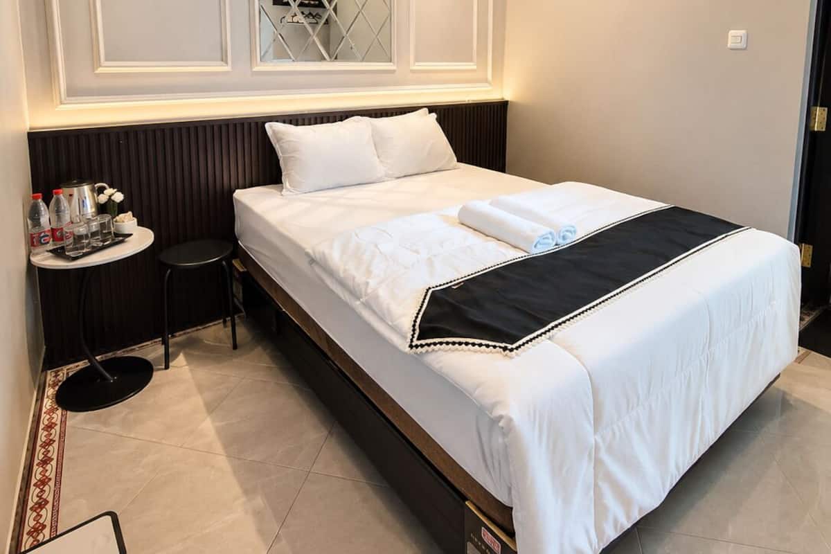 A neatly made bed with a black and white bedspread, a small round table with a tray of items, and a mirror above the bed.