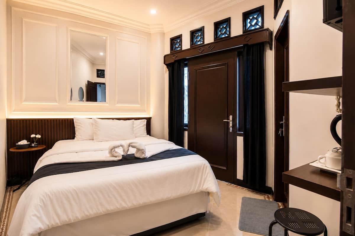 A hotel room with a large bed, a nightstand, a desk, a mirror, and a wardrobe.
