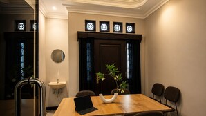 Un comedor con mesa de madera, cuatro sillas, una computadora portátil, un florero con flores, un lavamanos pequeño y una lámpara decorativa en el techo.