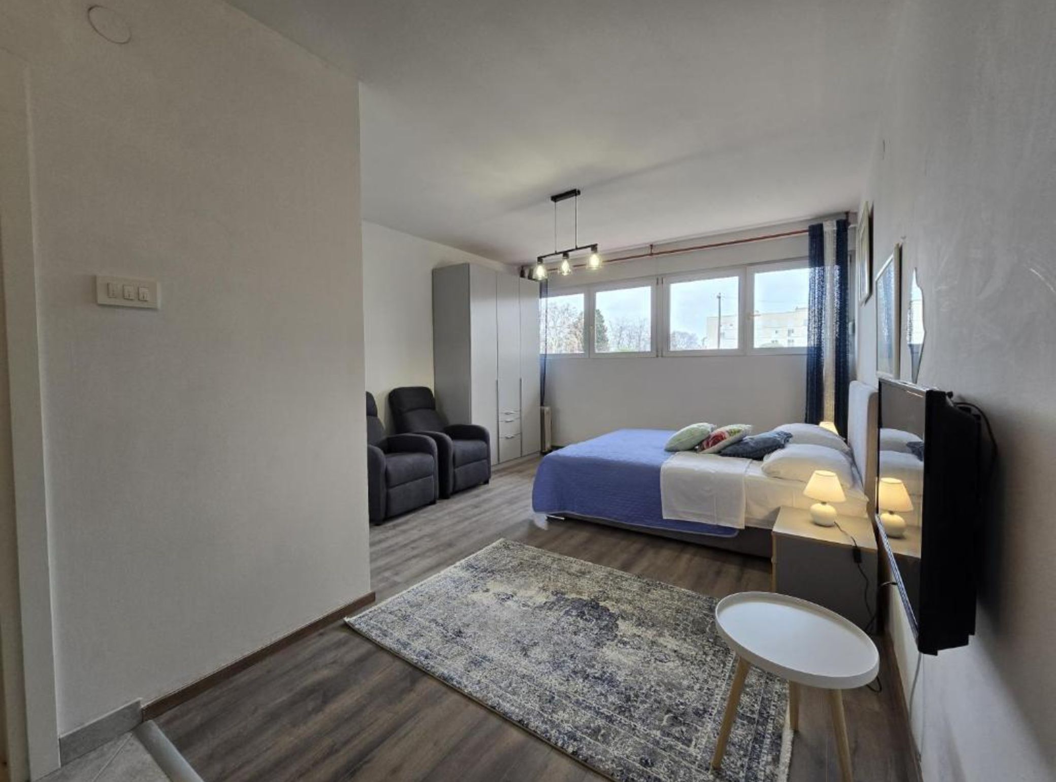 A bedroom with a bed, two chairs, a small table, a mirror, and a window.