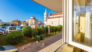 A view from a window overlooking a street with parked cars, a church, and a building with a dome. - Apartment Antonella (Zadar)