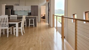 Una cocina moderna con armarios blancos, un comedor con sillas blancas y vistas al exterior a través de amplios ventanales.