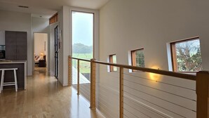 Una habitación amplia con piso de madera, una zona de cocina y ventanas grandes que ofrecen vistas al exterior.