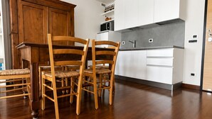 A modern kitchen with white cabinets, a wooden dining table with chairs, and a wooden cabinet. - Elegant apartment with a garage, two bedrooms, two bathrooms, and two terraces (Alba)