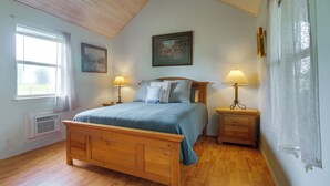 A bedroom with a wooden bed, two bedside tables with lamps, a window with curtains, a radiator, and a framed picture on the wall. - Cast & Relax! Wolf Creek Fishing Cabin w/ Dock (Grove)