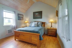 Ein Schlafzimmer mit einem Holzbett, zwei Nachttischen mit Lampen, einem Fenster mit Vorhängen, einer Heizung und einem gerahmten Bild an der Wand.