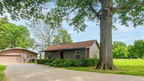 A single-story house with a garage, a driveway, and a large tree in front. - Cast & Relax! Wolf Creek Fishing Cabin w/ Dock (Grove)