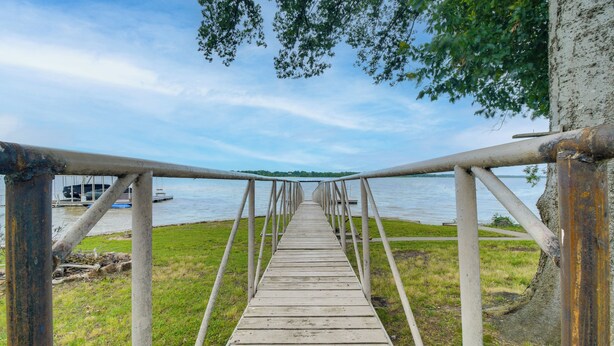 A wooden pier leading to a body of water with a boat docked nearby. - Cast & Relax! Wolf Creek Fishing Cabin w/ Dock (Grove)