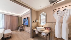 Un baño de hotel moderno con un espejo grande, un tocador con lavabo, una televisión y una zona de estar.
