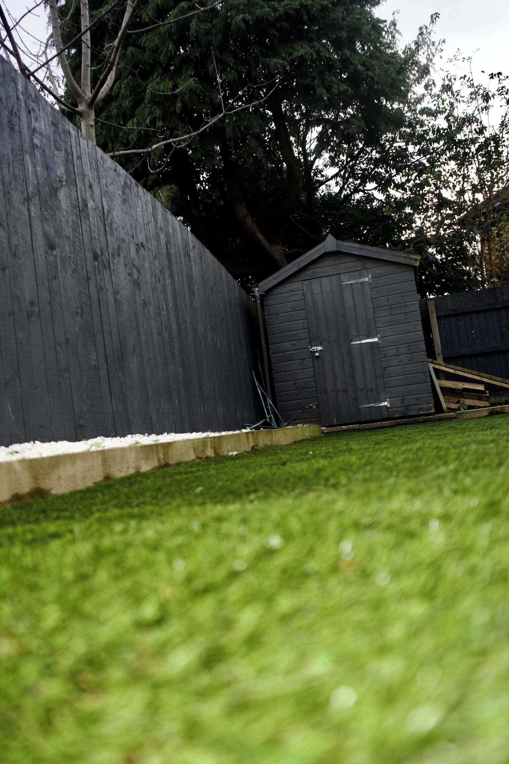 A backyard with a wooden fence, a shed, and a tree.