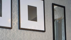 A neatly made bed with a tufted headboard, framed artwork on the wall, and a large mirror.