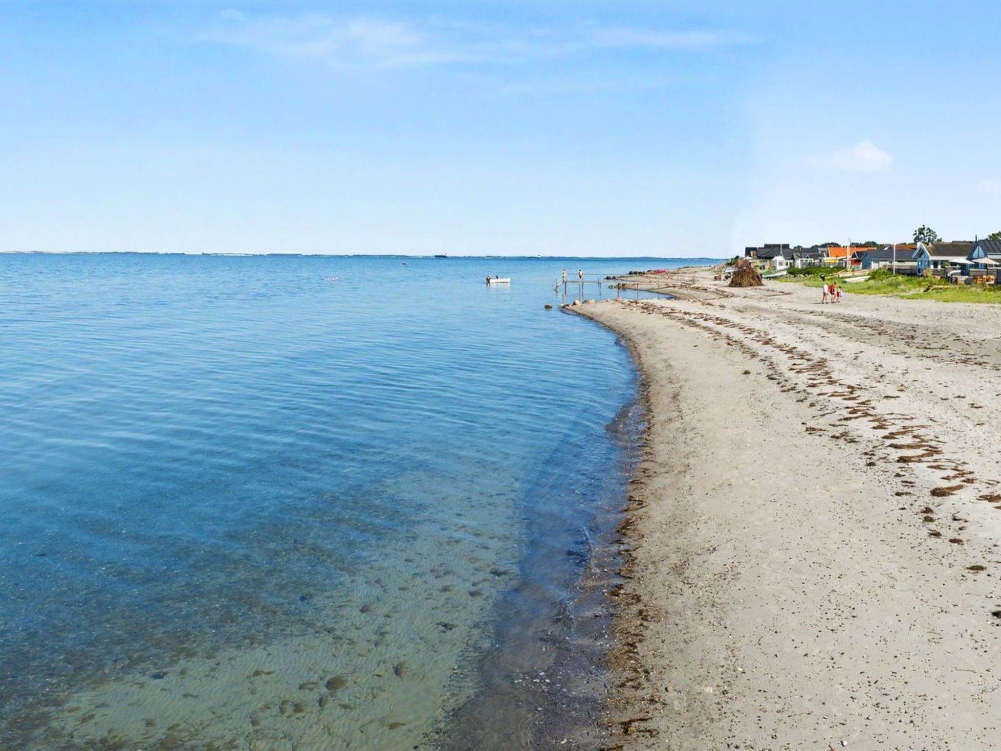 Une plage à l’eau claire, avec un rivage sablonneux et des maisons en arrière-plan.