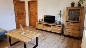 Uma sala de estar com uma mesa de madeira, uma TV sobre um móvel de madeira e um sofá azul.