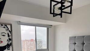 A modern bedroom with a large bed, a view of the city, and a painting on the wall.