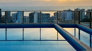 A rooftop pool with a cityscape view during sunset.