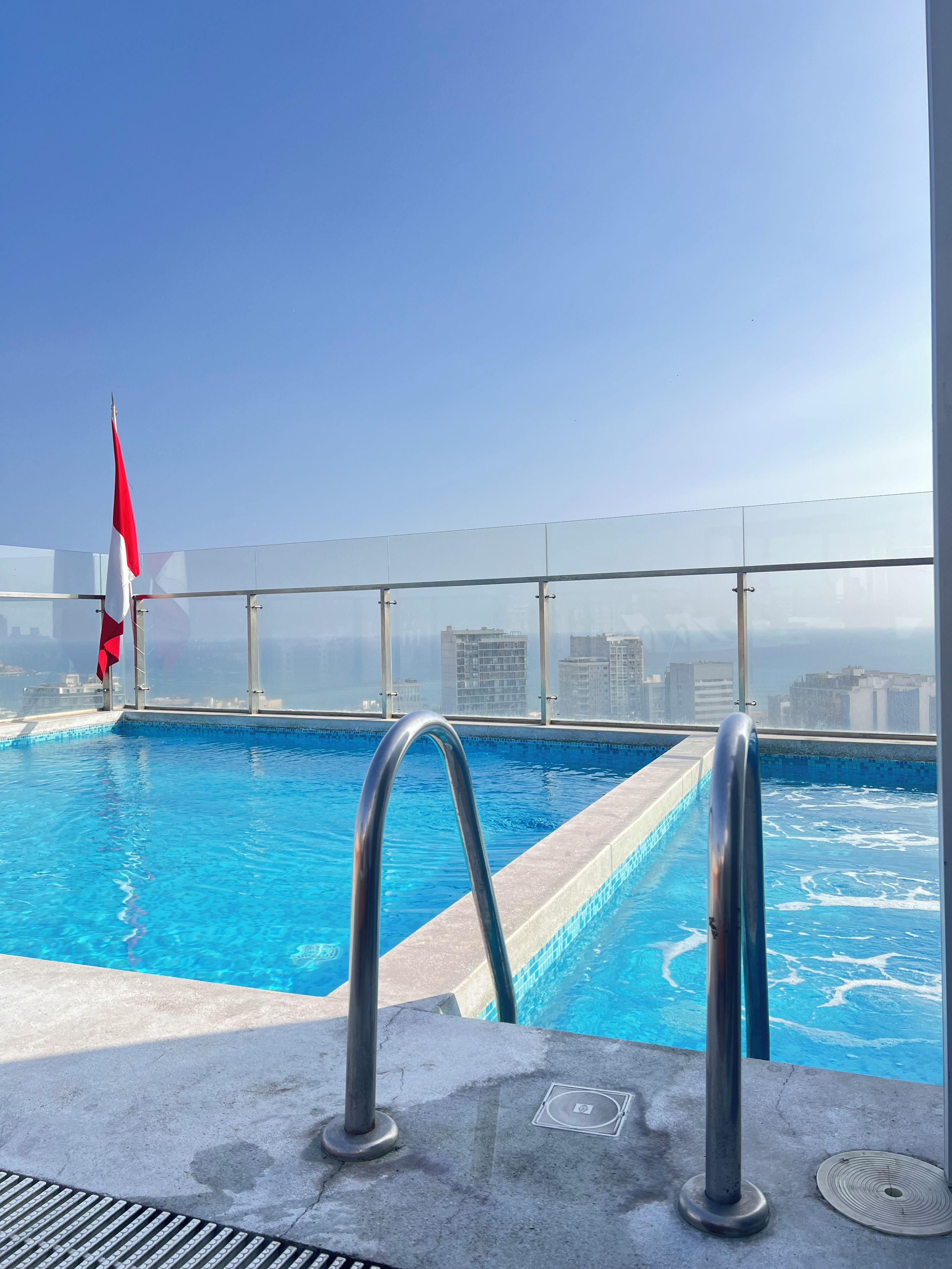 Piscina no terraço com água azul cristalina, grades de metal e uma bandeira.