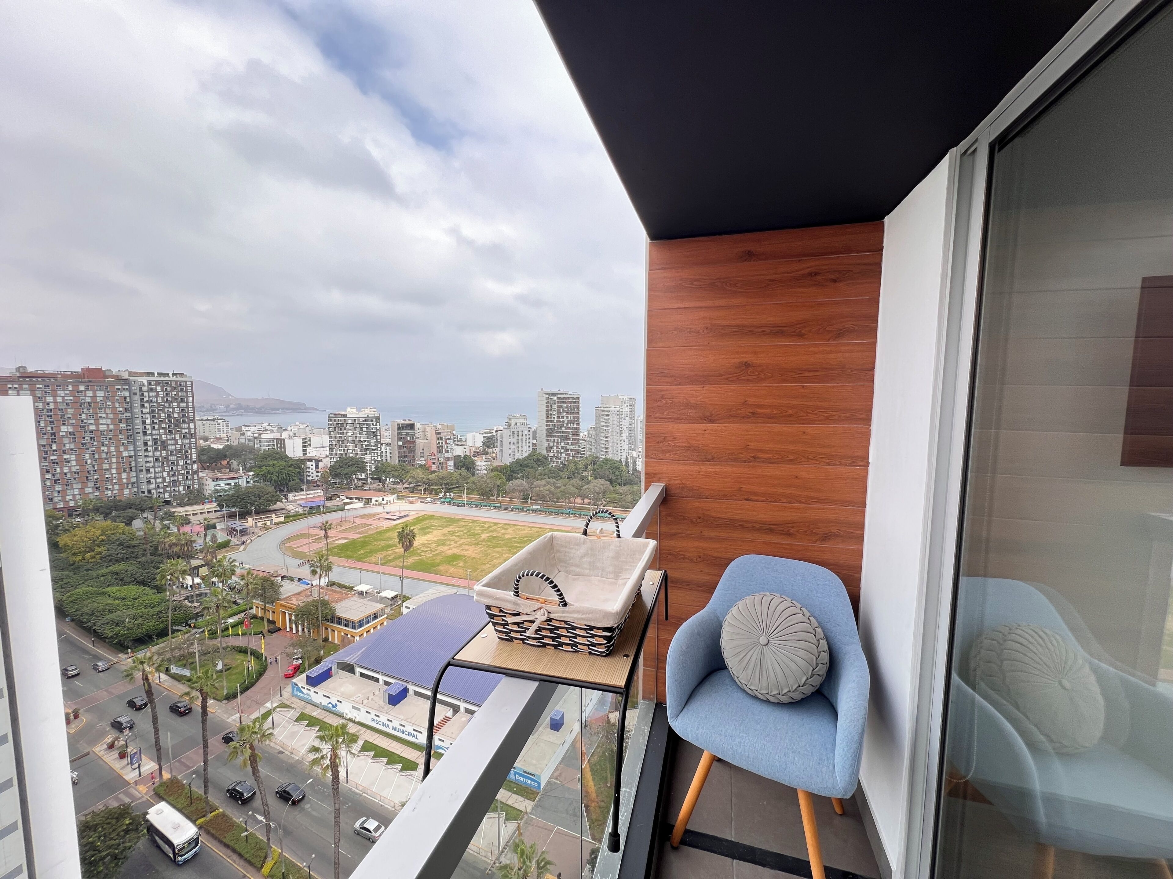 A balcony with a view of a cityscape, a chair, and a small table with a cushion.