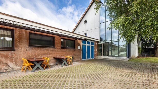 A building with a brick facade, a glass entrance, and a paved courtyard with outdoor seating. - Apartment 'Zwei Betten Studio' with Wi-Fi (Lübeck)