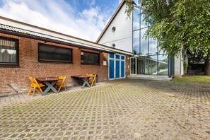 A building with a brick facade, a glass entrance, and a paved courtyard with outdoor seating. - Apartment 'Zwei Betten Studio' with Wi-Fi (Lübeck)