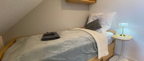 Ein Schlafzimmer mit einem Bett, einem Nachttisch mit Lampe, einem Regal über dem Bett und Holzboden.