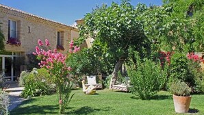 A stone building with a garden featuring a pergola, flowering plants, and a bird sculpture.