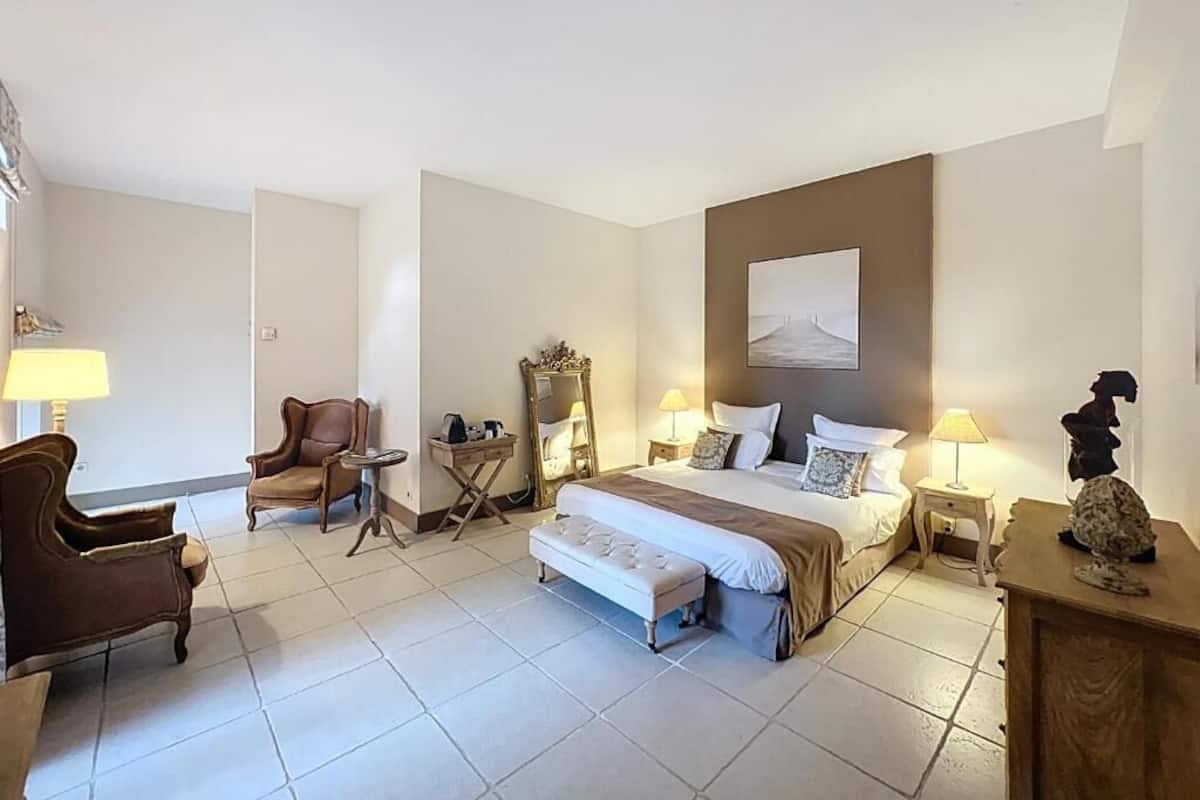 Una habitación de hotel con una cama, una silla, una mesita, un banco y una lámpara.