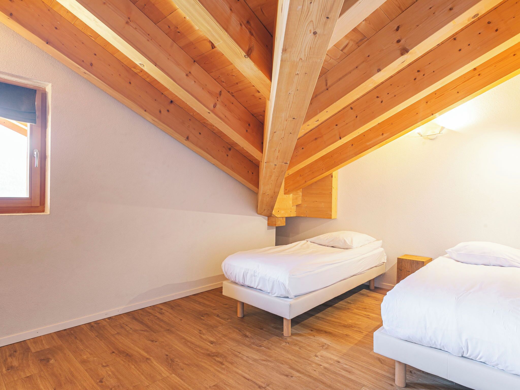 Une chambre avec deux lits, des poutres en bois, une fenêtre et un luminaire.