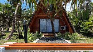 A wooden cabin with a large window, surrounded by tropical vegetation. - FAMILY BUNGALOW: E-FRAME HOUSE Facing the Ocean (Toamasina)