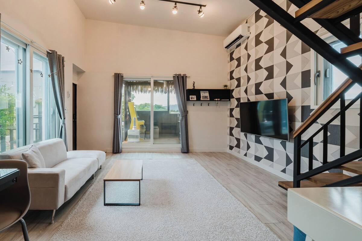 Una sala de estar moderna con un sofá, un televisor, un escritorio y una escalera.