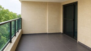 A balcony with a tiled floor, glass doors, and a view of trees.