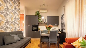 En moderne stue med sofa, spisebord, stole og et tekøkken.