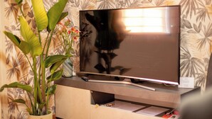 Et fladskærms-tv på et træskab med blomstret tapet i baggrunden.