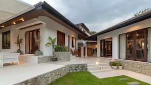 A modern house with a stone pathway, a white bench, and potted plants.