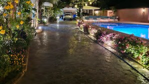 A nighttime pathway leading to a pool area with a car parked in the background.