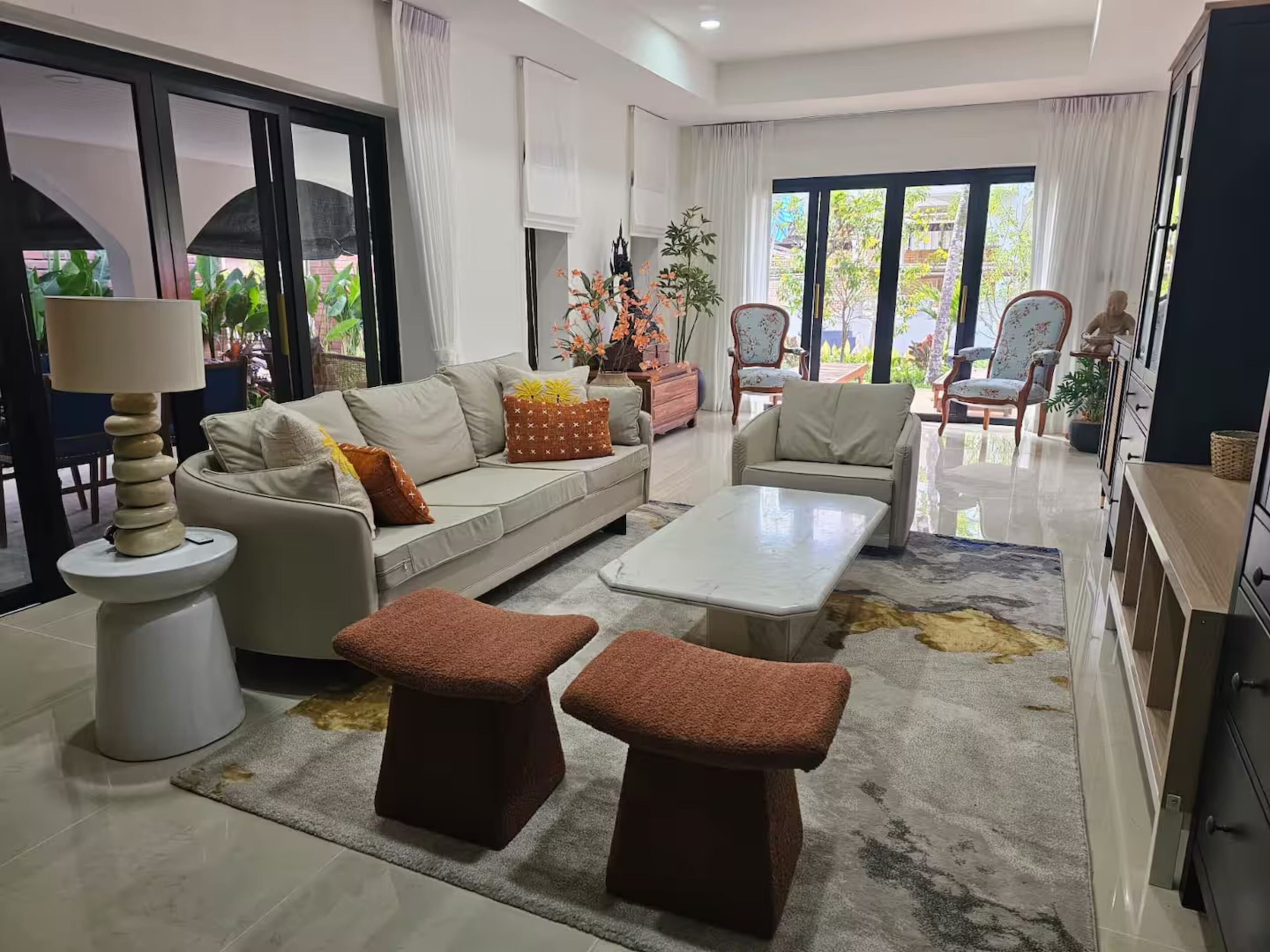 A modern living room with a sofa, coffee table, ottomans, and a lamp.